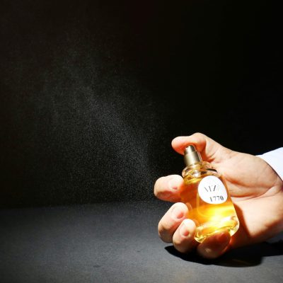 Hand holding a perfume bottle spraying mist against a dark backdrop for a classy vibe.